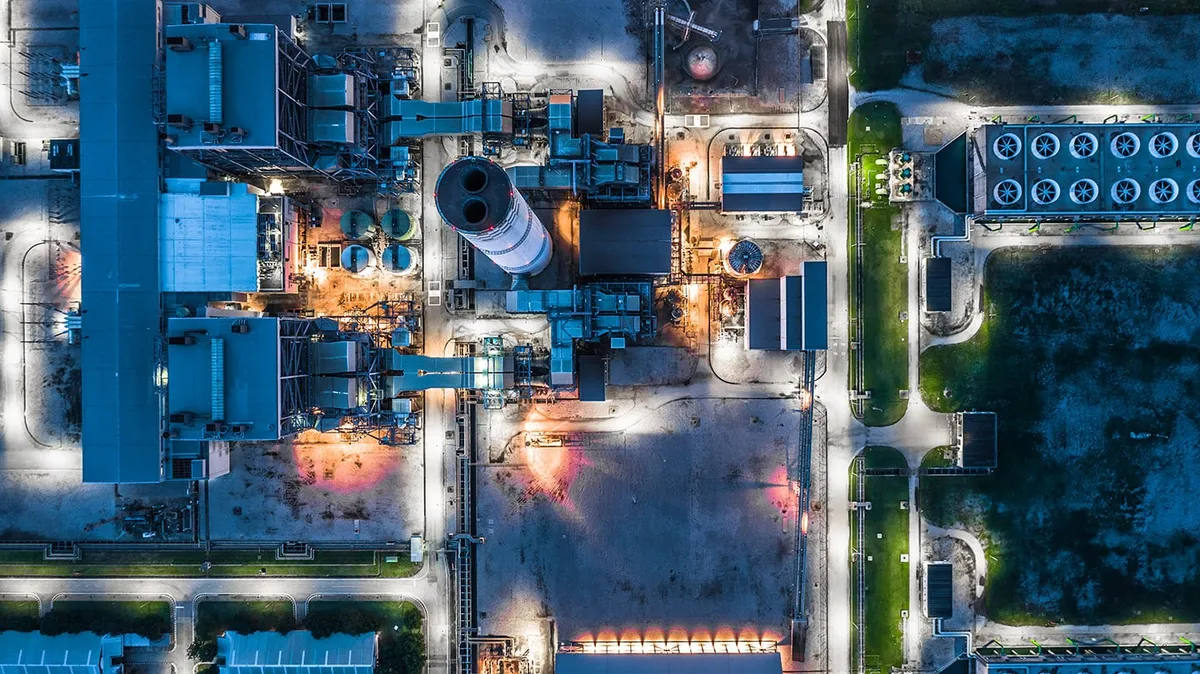 Aerial night view of a power plant complex with lit buildings, a stack and cooling units