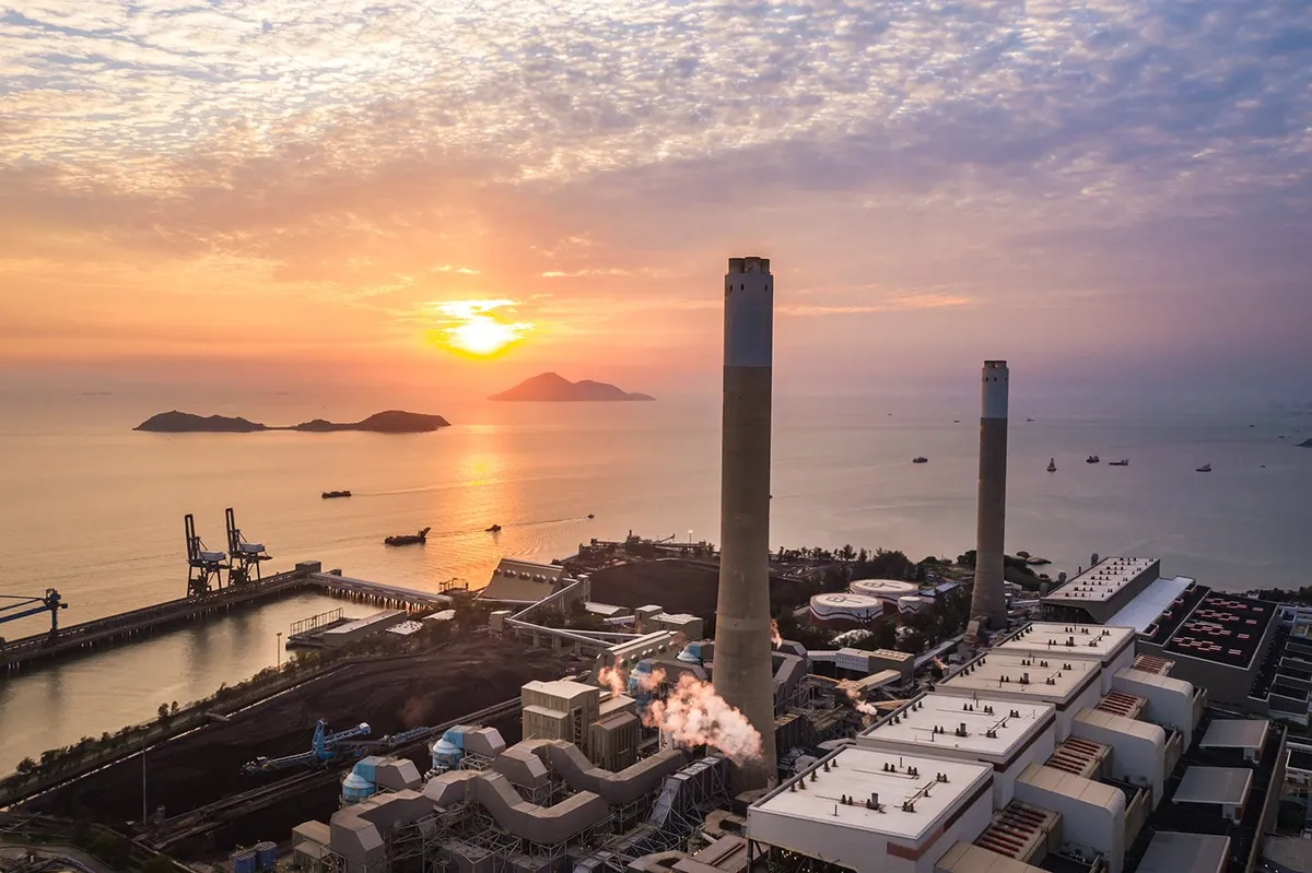 Waterfront power plant with two tall smokestacks and dock cranes at sunset