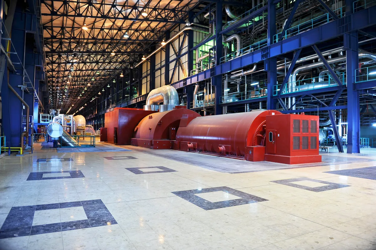 Large red turbine generator on a tiled floor inside a power plant hall