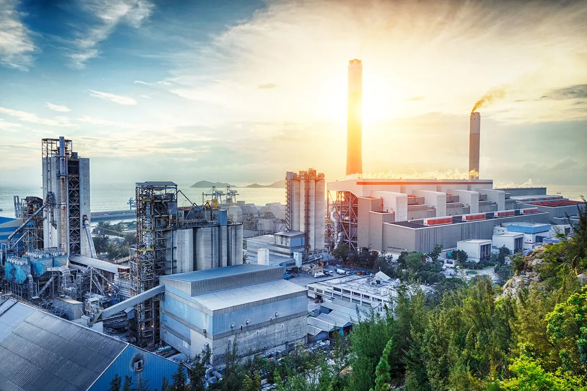 Industrial power plant with tall smokestacks and the setting sun glowing behind them
