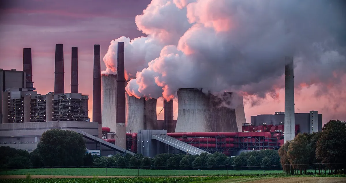 Power station with tall chimneys and cooling towers releasing steam into a pink dusk sky