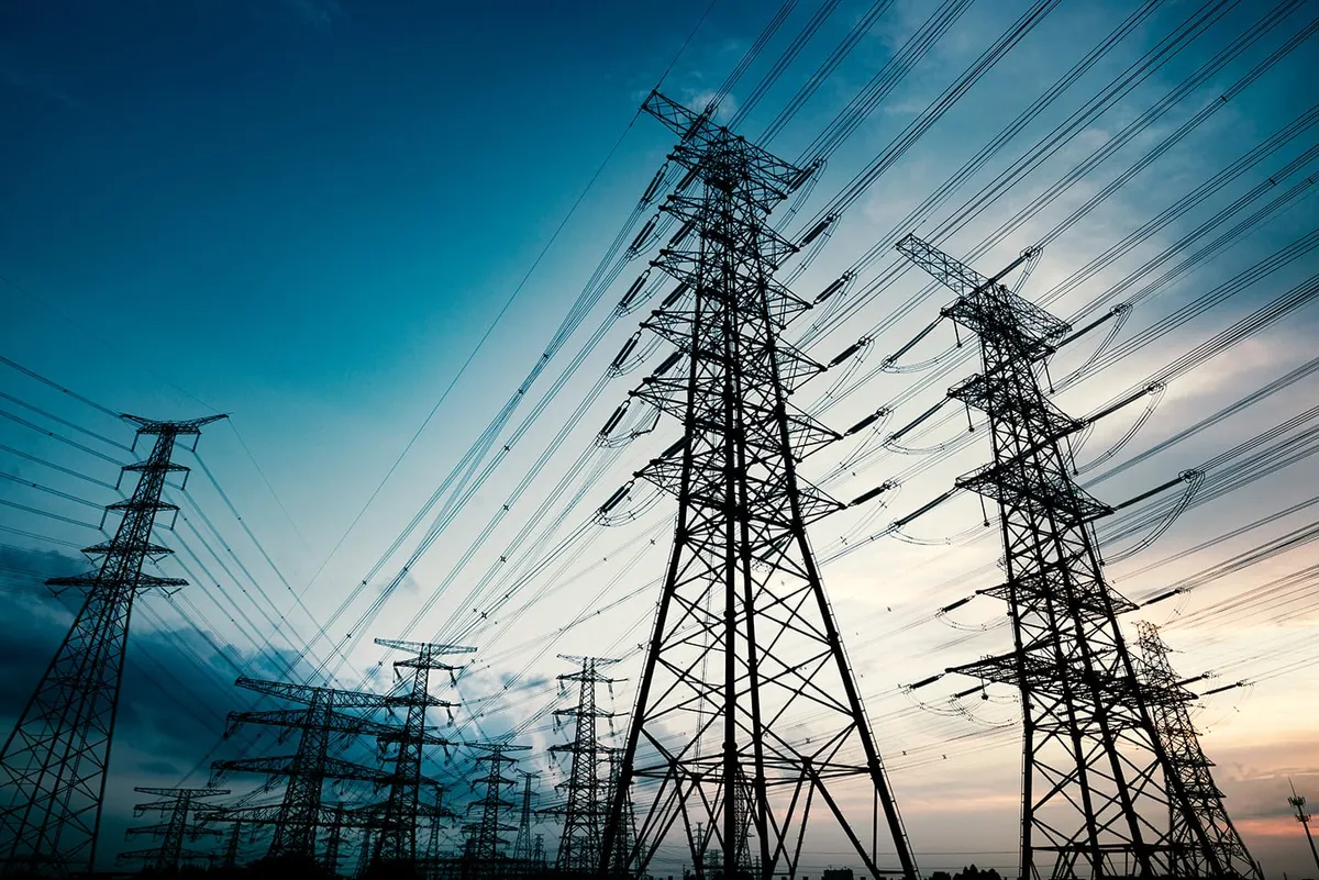 Rows of high-voltage pylons and cables seen from below against a teal sky