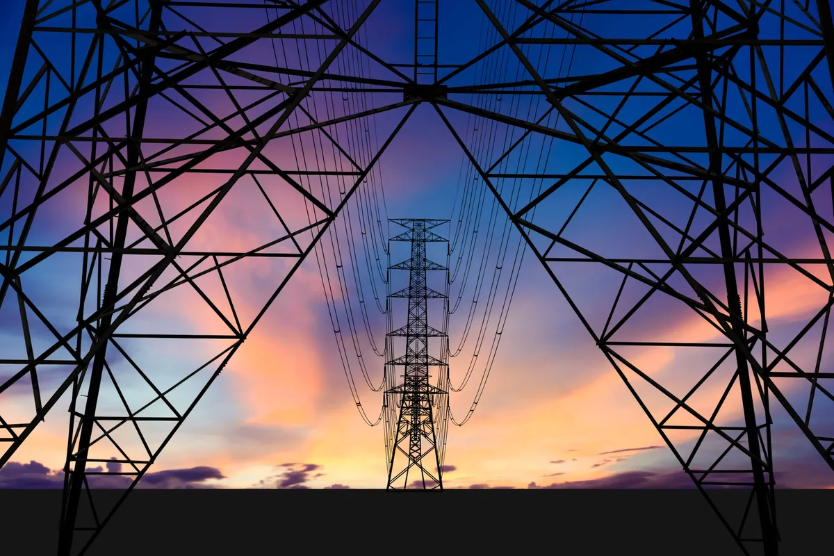 Steel transmission towers framing a distant pylon against a purple and orange sunset sky