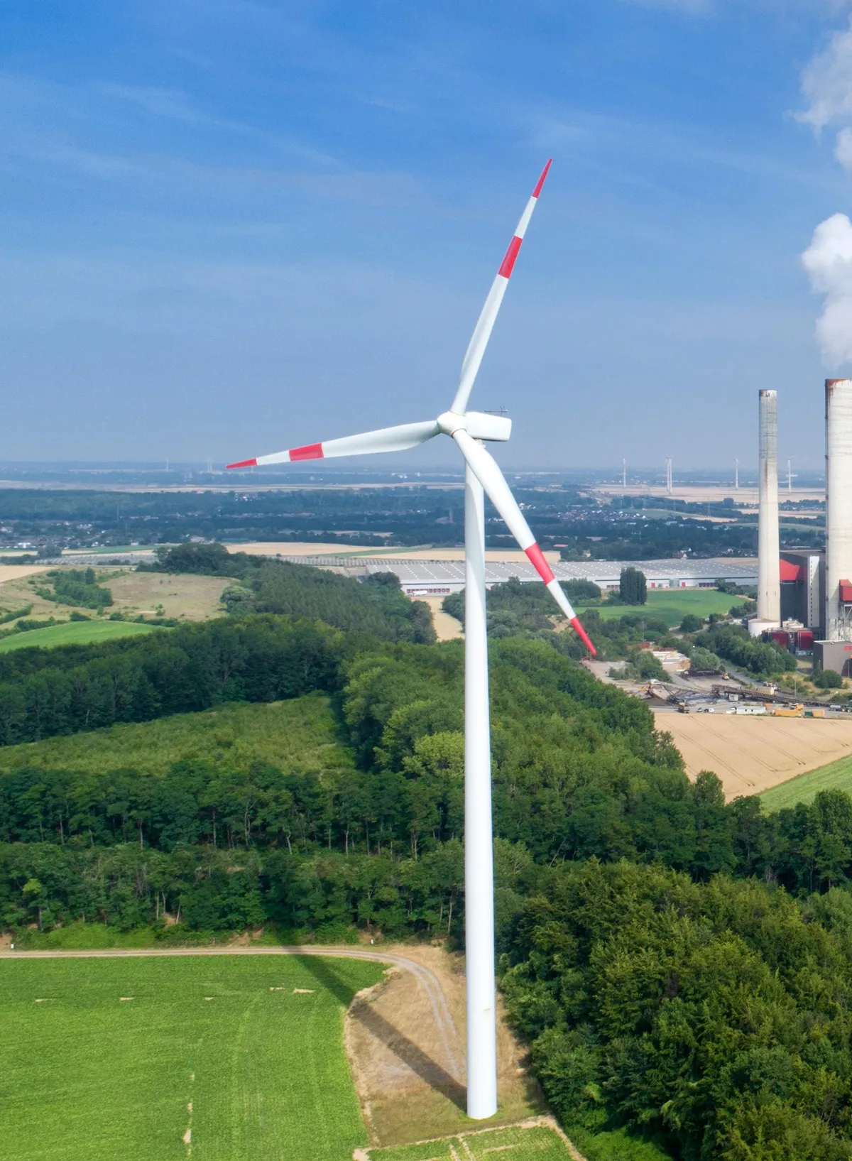 Wind turbine in green countryside with a power plant and steam plume in the distance