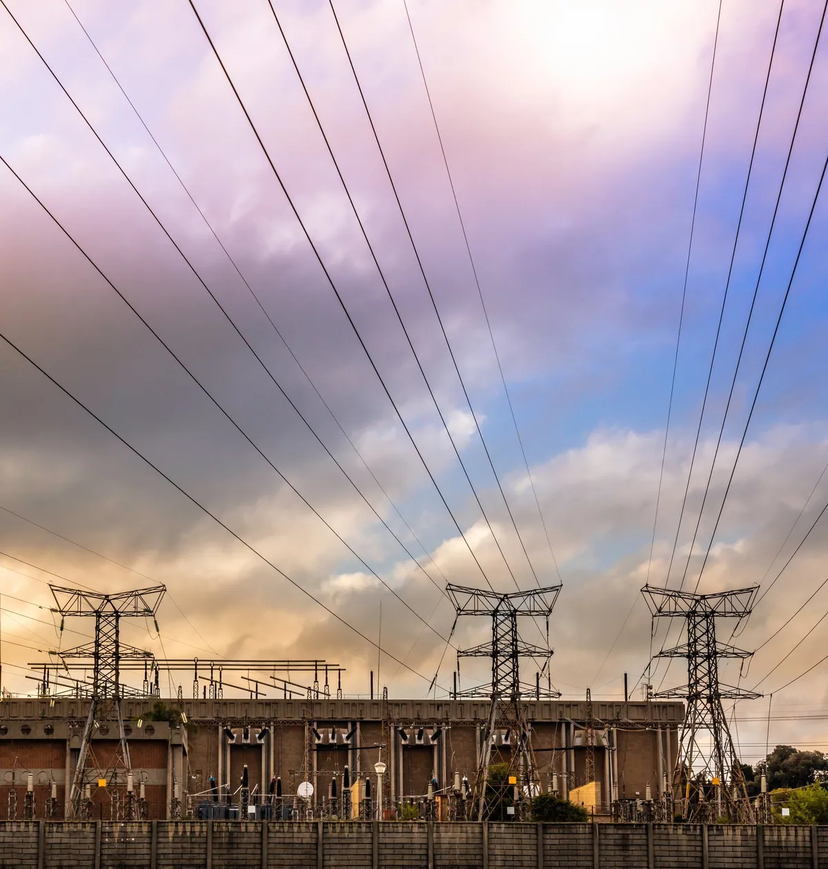 Power lines converging on an electrical substation under a colorful cloudy sky