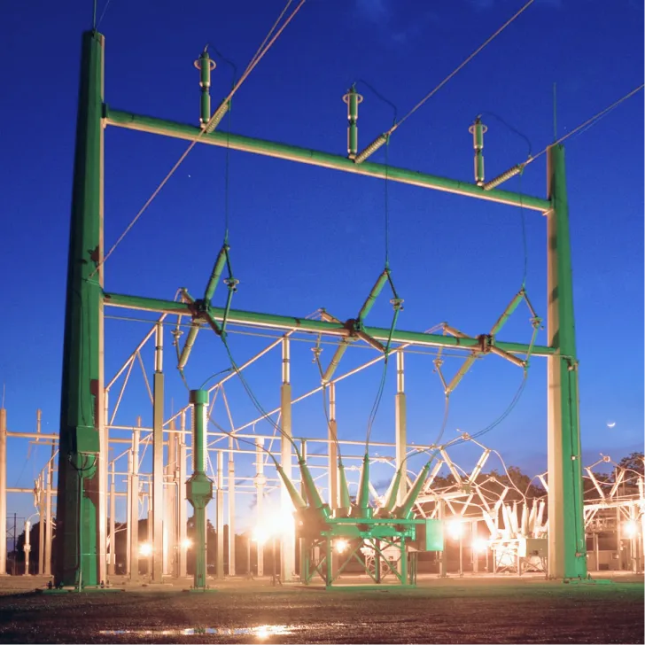 Green steel substation structure and insulators lit at dusk against a deep blue sky